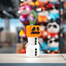 Load image into Gallery viewer, Minecraft 5 Inch Snow Golem Bag Hanger Plush with pixelated pumpkin head and clip, displayed on a table.