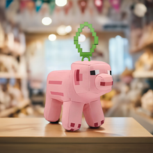 Load image into Gallery viewer, Minecraft 5 Inch Pig Bag Hanger Plush showcasing pixelated details and clip attachment on wooden surface.