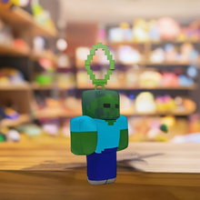 Load image into Gallery viewer, Minecraft 5 Inch Zombie Bag Hanger Plush with pixelated design on a wooden table in toy store.
